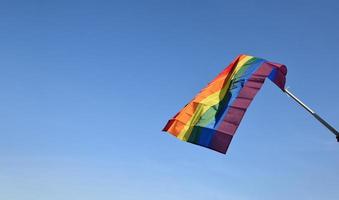 bandera del arco iris sosteniendo en la mano contra el fondo del cielo azul, concepto para la celebración lgbt en el mes del orgullo, junio, en todo el mundo. foto