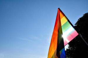 bandera del arco iris sosteniendo en la mano contra el fondo del cielo azul, concepto para la celebración lgbt en el mes del orgullo, junio, en todo el mundo. foto