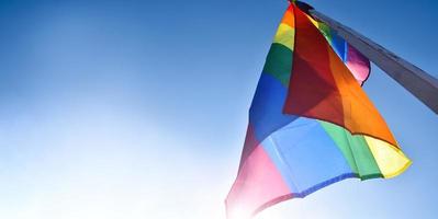 Look up view of rainbow flag, LGBT simbol, against clear bluesky background, soft and  selective focus, concept for LGBT celebration in pride month, June, around the world, copy space. photo