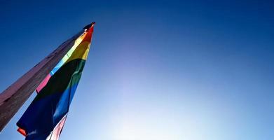 Look up view of rainbow flag, LGBT simbol, against clear bluesky background, soft and  selective focus, concept for LGBT celebration in pride month, June, around the world, copy space. photo