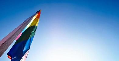 Look up view of rainbow flag, LGBT simbol, against clear bluesky background, soft and  selective focus, concept for LGBT celebration in pride month, June, around the world, copy space. photo