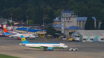 sochi, rússia, 30 de julho de 2022 - trator rebocando airbus a320 214, uk32015 do uzbequistão expresso para a pista de táxi ou pista para o aeroporto de sochi. conceito de turismo e viagens video