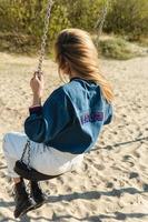 foto trasera de una mujer joven columpiándose en un columpio en la playa.