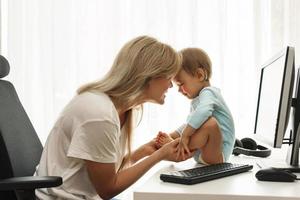 Young freelancer mother playing with little son in home office. photo