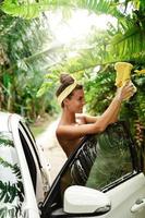 Attractive woman wearing red bikini is washing her white car in backyard photo