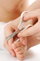 Mother holding little child's foot and cutting toenails. photo