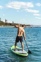 Young male surfer riding standup paddleboard in ocean. photo