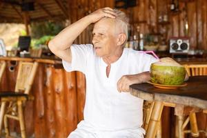 un anciano feliz está bebiendo agua de coco en el bar de la playa foto