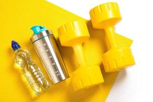 Yellow dumbbells, fitness mat, bottle of water and protein shaker photo