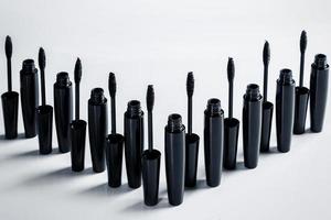 Black mascara brushes and containers on white background photo