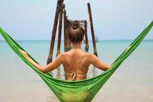 Woman is relaxing in the hammock hanging on old beams from the broken pier photo