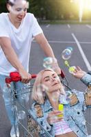 la pareja se divierte con un carrito de compras y hace burbujas en el estacionamiento de un supermercado