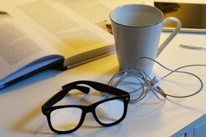 objetos en el escritorio - taza de bebida caliente, gafas, libros y auriculares foto