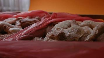 Close-up view of hands in gloves packing chicken legs from a box into individual plastic bags. Process of freezing meat for further use at home. 4k video with light play