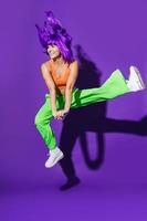 Carefree woman dancer wearing colorful sportswear having fun against purple background photo