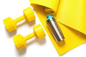 Yellow dumbbells and protein shaker on the fitness mat photo