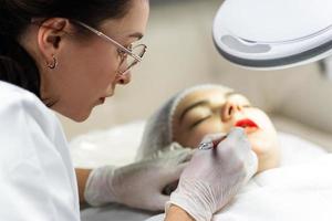 Permanent makeup artist and her client during lip blushing procedure photo