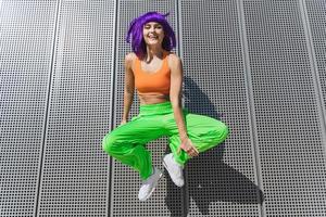 Carefree woman wearing colorful sportswear jumping on the street during summer day photo
