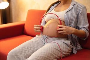 Pregnant woman belly with a red headphones photo