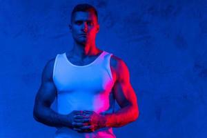 Handsome and confident bodybuilder posing in colorful light photo