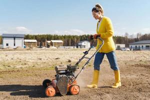 Woman villager is using aerator machine to scarification and aeration of lawn or meadow photo