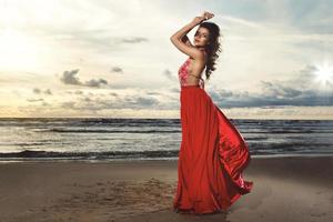 impresionante mujer con un hermoso vestido rojo en la playa foto