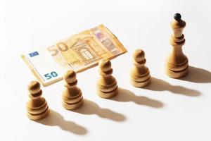 Fifty euro banknote and row of wooden chessmen. photo