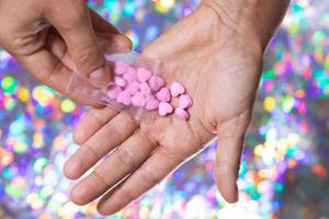 Man pouring heart shaped pills on palm from ziplock bag. photo