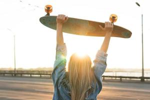 Carefree woman with a longboard on a bridge at sunset photo