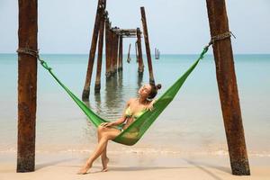 Woman is relaxing in the hammock hanging on old beams from the broken pier photo