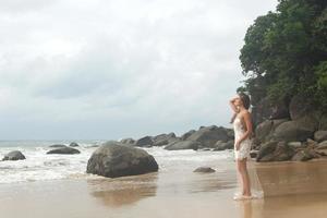 Young woman wearing beautiful white dress is posing on the beach photo