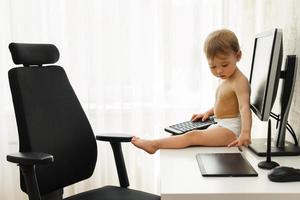 Little boy sitting on a desk and playing with a keyboard. photo