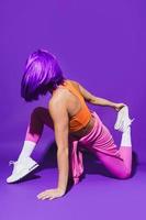 Woman wearing colorful sportswear during stretching workout against purple background photo