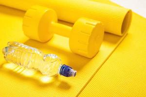 Yellow dumbbell, fitness mat and bottle of still water photo