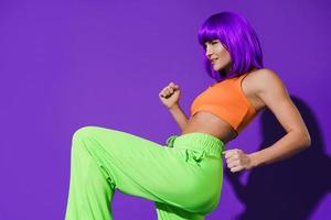 Carefree woman dancer wearing colorful sportswear having fun against purple background photo