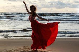 impresionante mujer con un hermoso vestido rojo en la playa foto