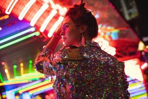 Stylish woman wearing jacket with shining sequins on the city street with neon lights photo