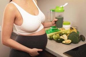 mujer embarazada sosteniendo un agitador con un cóctel de proteína verde foto