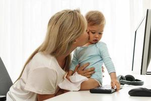 Young freelancer mother kissing son in home office. photo