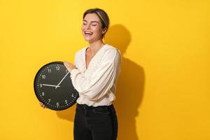 mujer alegre sosteniendo un gran reloj de fondo amarillo foto