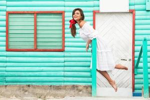 Cute woman wearing beautiful white dress is posing near colorful wooden house photo