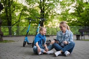 madre e hija usando una aplicación en un teléfono inteligente para compartir scooters eléctricos foto