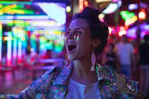 mujer elegante con chaqueta con lentejuelas brillantes en la calle de la ciudad con luces de neón foto