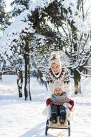 la madre y su pequeño y lindo hijo se divierten en una colina de trineo durante el soleado día de invierno foto