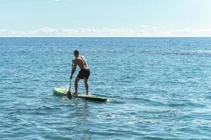 joven surfista masculino montando paddleboard de pie en el océano. foto