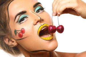 hermosa modelo con maquillaje creativo de arte pop está comiendo cerezas foto