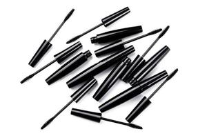 Black mascara brushes and containers on white background photo