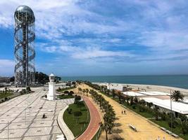 A large beautiful metal modern spiral high architecture tower alphabet, a symbol of the city and glass booms, buildings, skyscrapers on the coast. Batumi, Georgia, April 17, 2019 photo