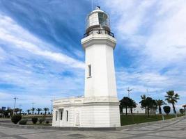 Big tall stone white lighthouse on the tropical sea warm summer resort with palm trees against the blue sky photo