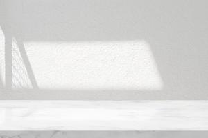 mesa de mármol blanco con fondo de textura de pared de estuco con haz de luz y sombra de valla, adecuada para el telón de fondo de presentación del producto, exhibición y maqueta. foto
